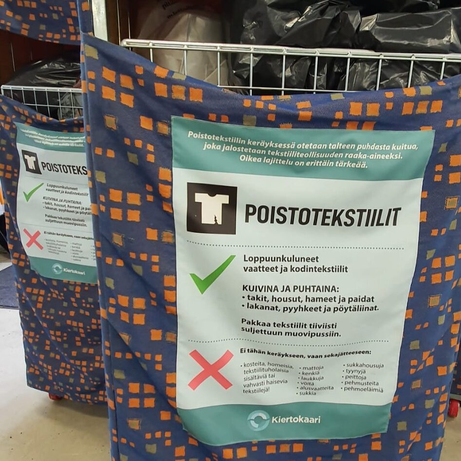 Poistotekstiilin keräysrullakkoja. Rullakot on verhoiltu värikkäällä kankaalla ja niihin on kiinnitetty lajitteluohje. 